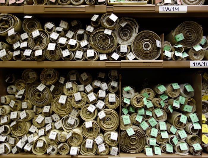 Shelves containing stacked scrolls of parchment featuring British laws