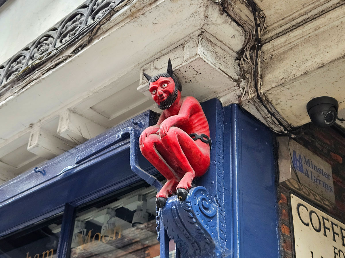 A red carved wooden devil sitting on a decorative wooden post on the side of a shop
