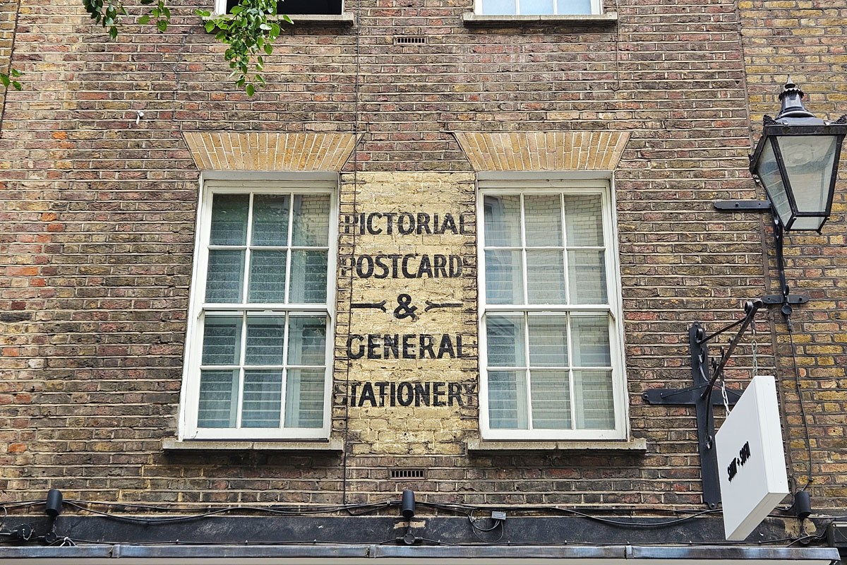 An old sign painted on a building between two windows. It reads: pictorial postcards and general stationery