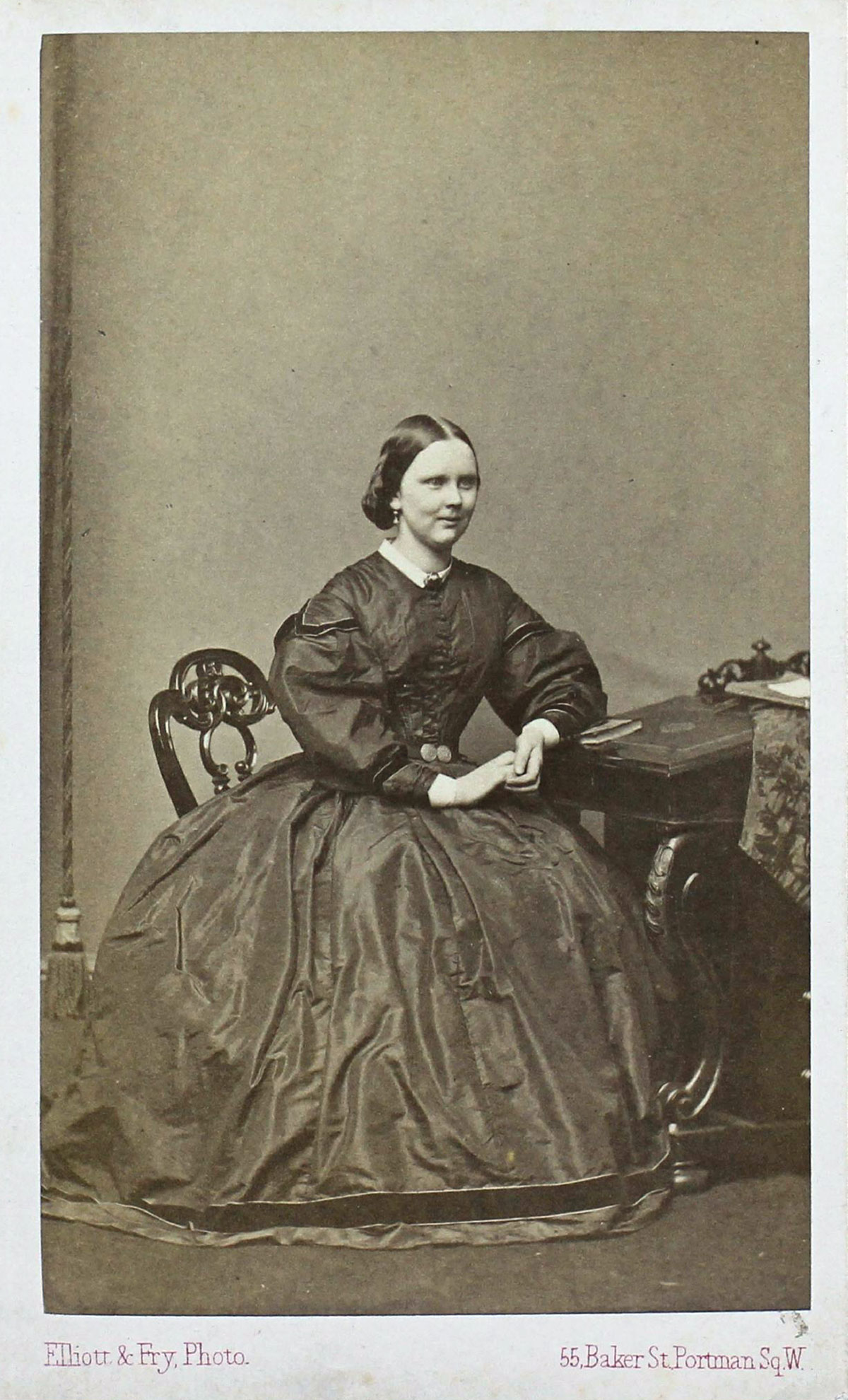 A sepia-toned photograph of a woman sitting at a desk wearing a full skirt