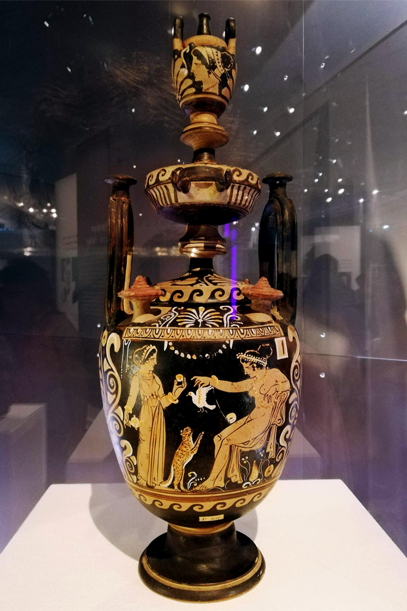 An ancient black and orange pot with a picture of a cat begging for a bird