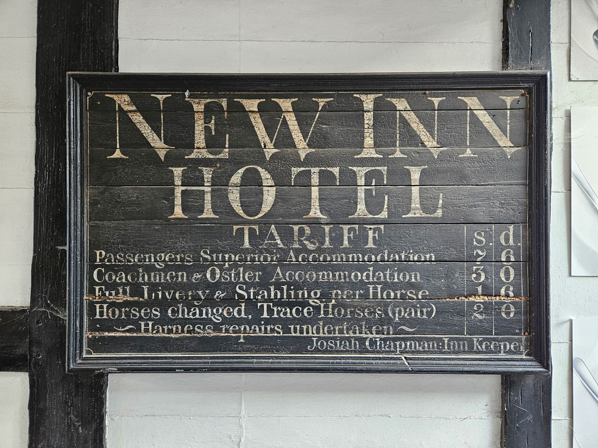 An old wooden sign showing prices for staying in a Tudor-era coaching inn.