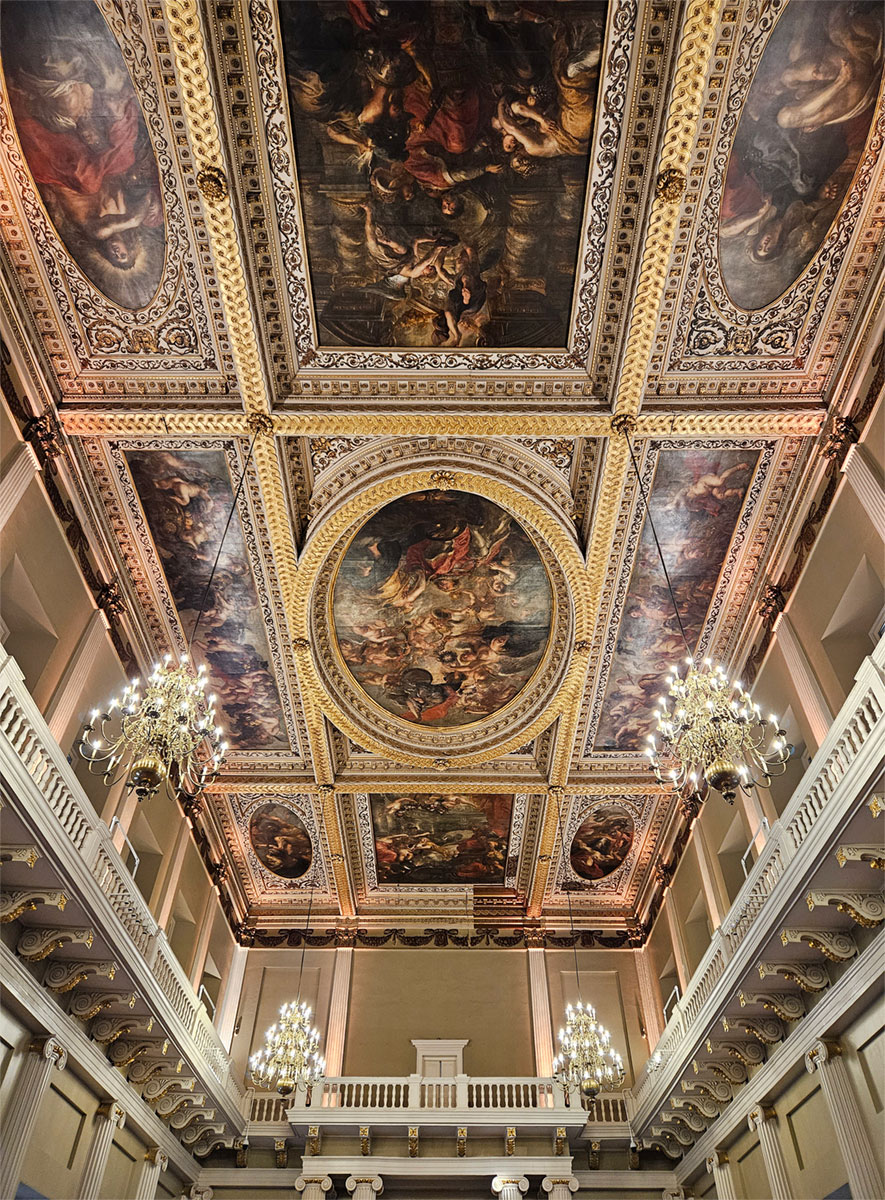 The painted ceiling of a grand room, with hanging chandeliers