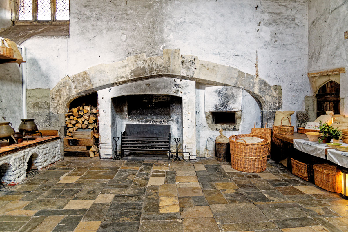 A Tudor-era kitchen with a fireplace on the far wall and benches on either side of the room
