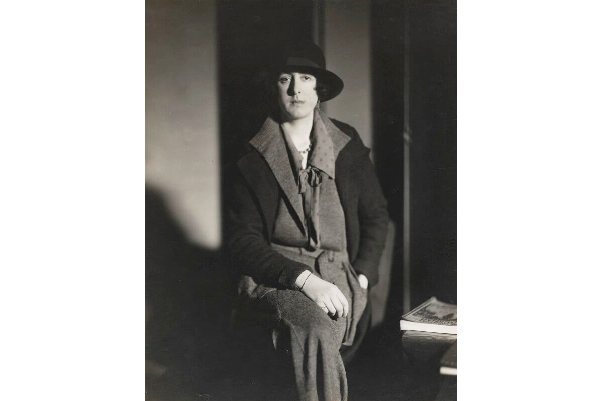 A black and white photograph of a woman sitting up straight, wearing a hat