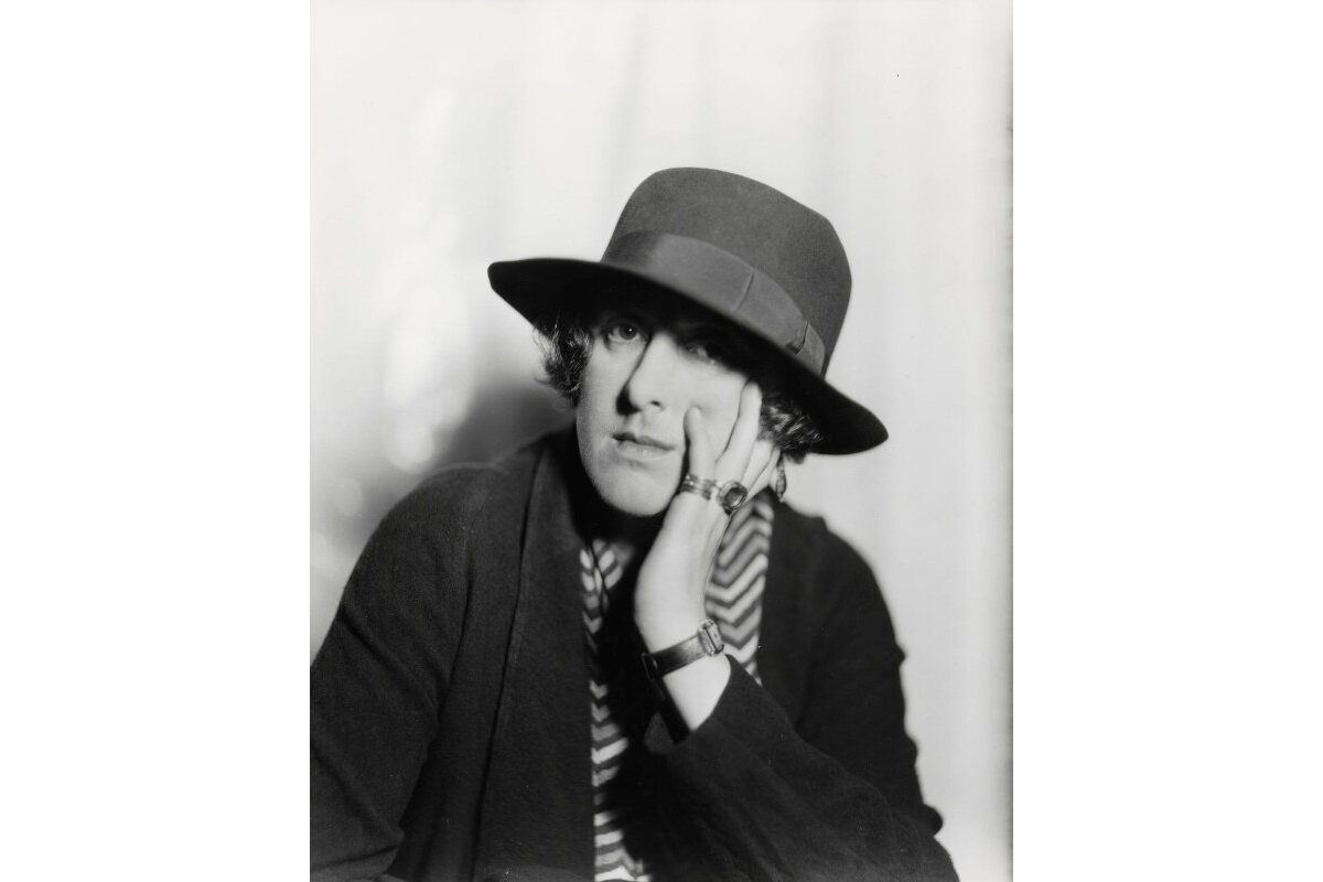 A black and white potography of a woman wearing a hat, resting her head on her hand