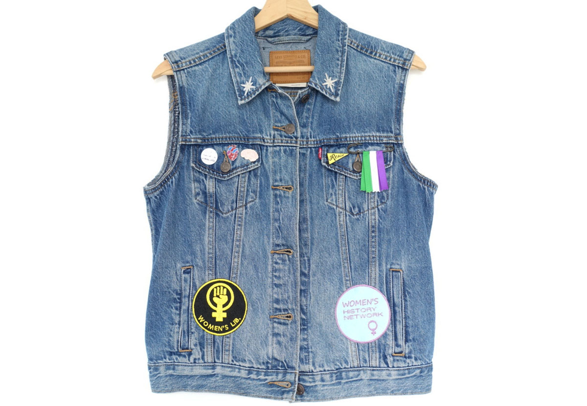 A sleeveless denim jacket decorated with embroidered patches, badges, and ribbons.
