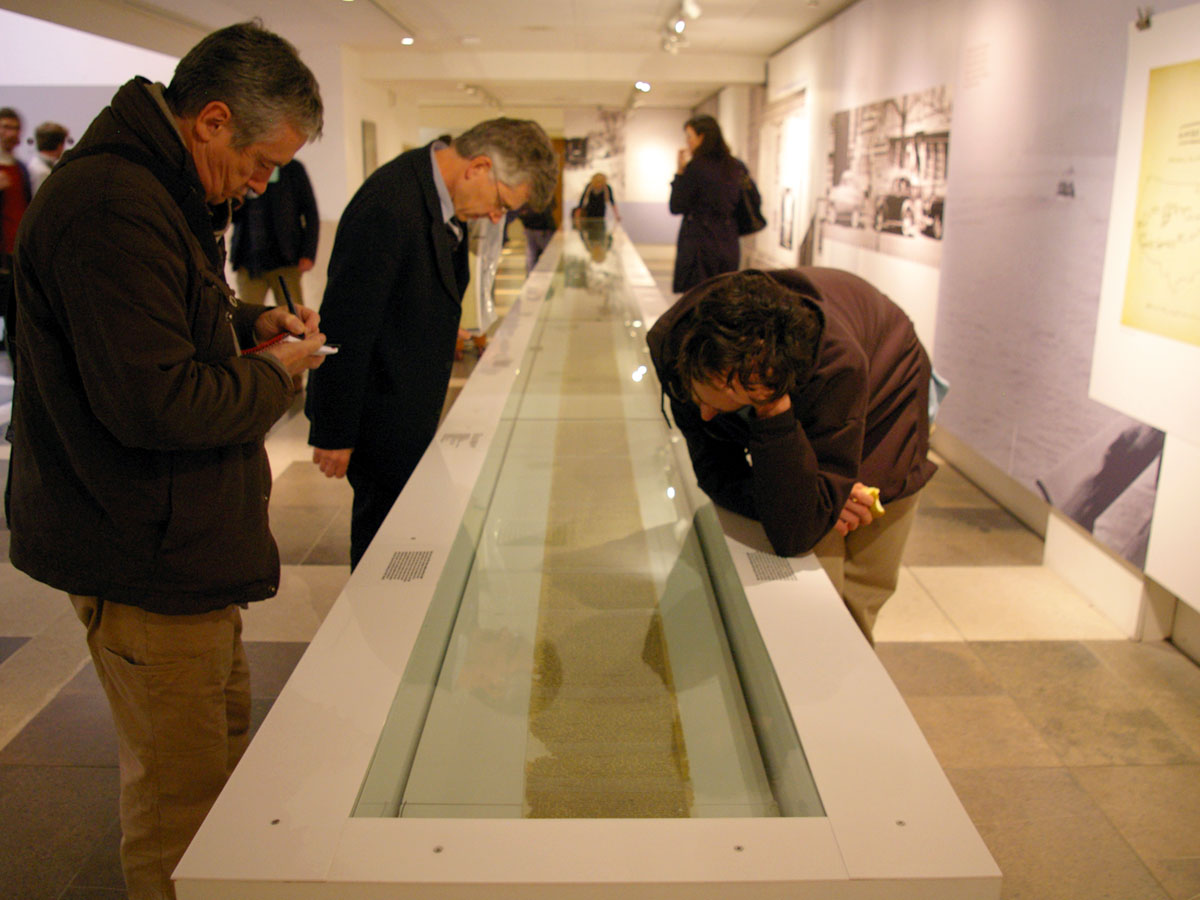A long display case holding a type-written manuscript, with several men bending over to read the writing